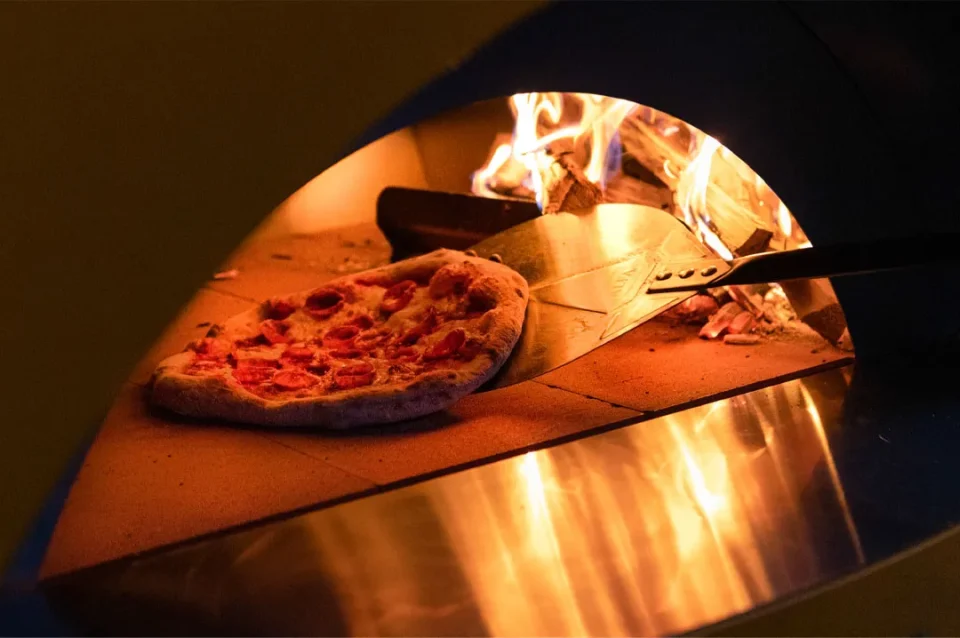 Pepperoni pizza sliding into one of our wood-fired outdoor pizza ovens