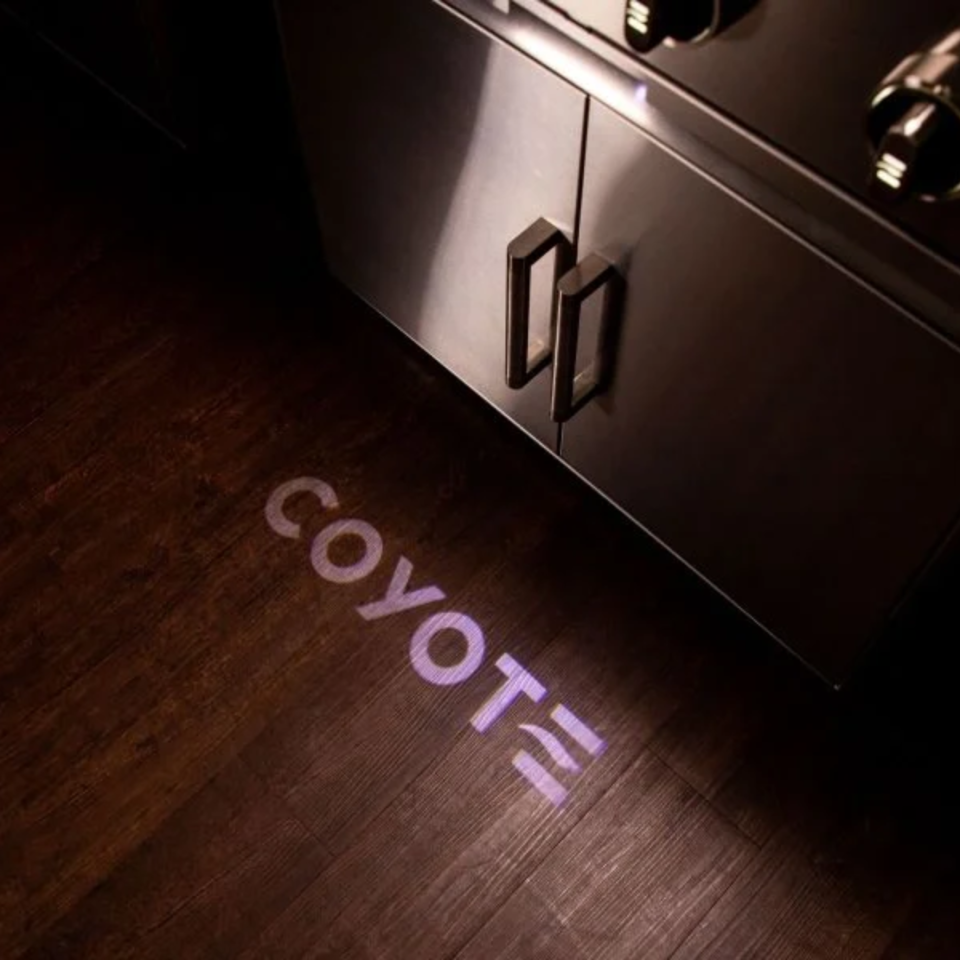 Coyote Grill Reviews – close-up of stainless steel grill cabinet with Coyote logo light projection, showcasing premium outdoor kitchen design.