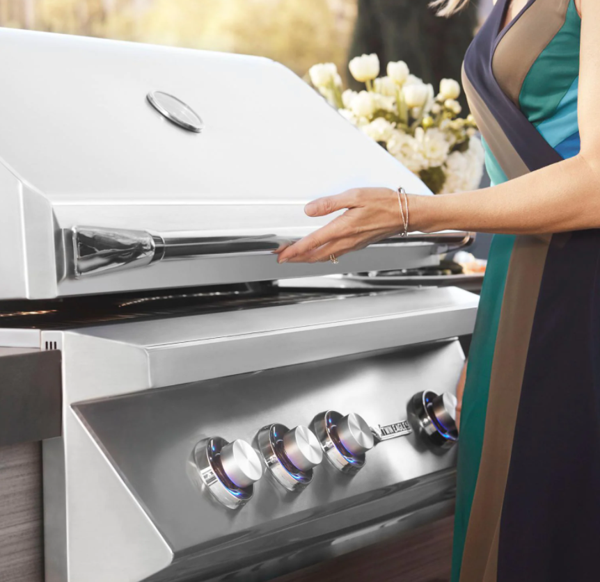 Woman opening a Twin Eagles built-in gas grill, showcasing premium stainless steel design and American craftsmanship.