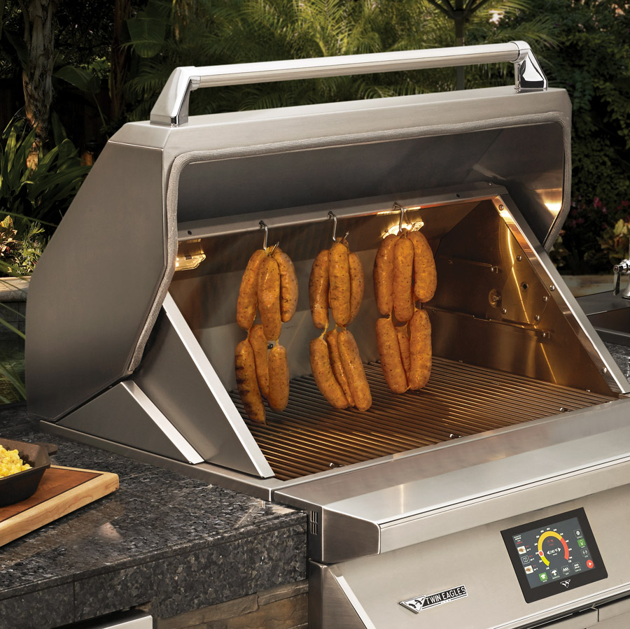 Twin Eagles built in pellet grill with digital touchscreen and stainless steel finish, shown smoking sausages in a custom outdoor kitchen island