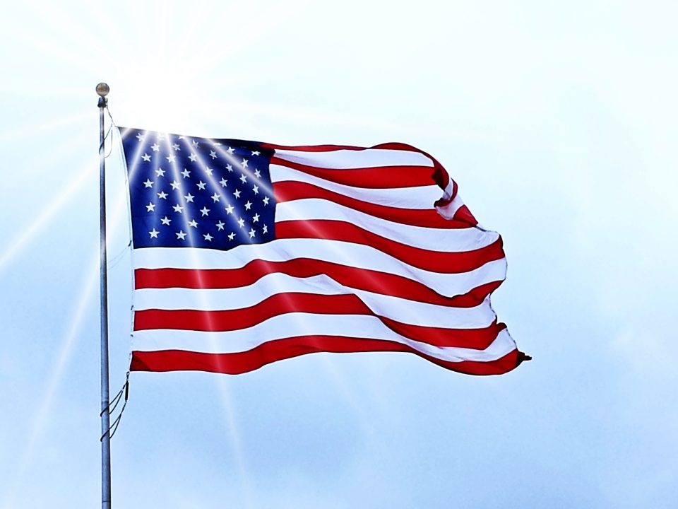 American flag waving proudly in the sunlight, symbolizing USA-made quality and craftsmanship behind AOG grills.