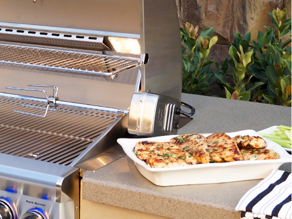 AOG grill with rotisserie motor and grilled chicken plated beside it, shown on a stone countertop.