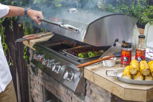 Bull Angus 30-inch built-in gas grill in use with BBQ sauces, grilled corn, and smoked ribs on the cooking surface.
