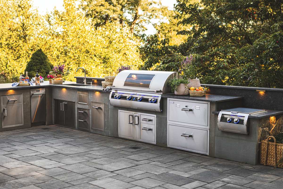 Fire Magic outdoor kitchen with built-in grill, side burner, drawers, and sink in a premium stainless steel island setup.