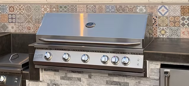 Close-up of KoKoMo built-in stainless steel grill installed in a custom outdoor kitchen with stone and tile backsplash
